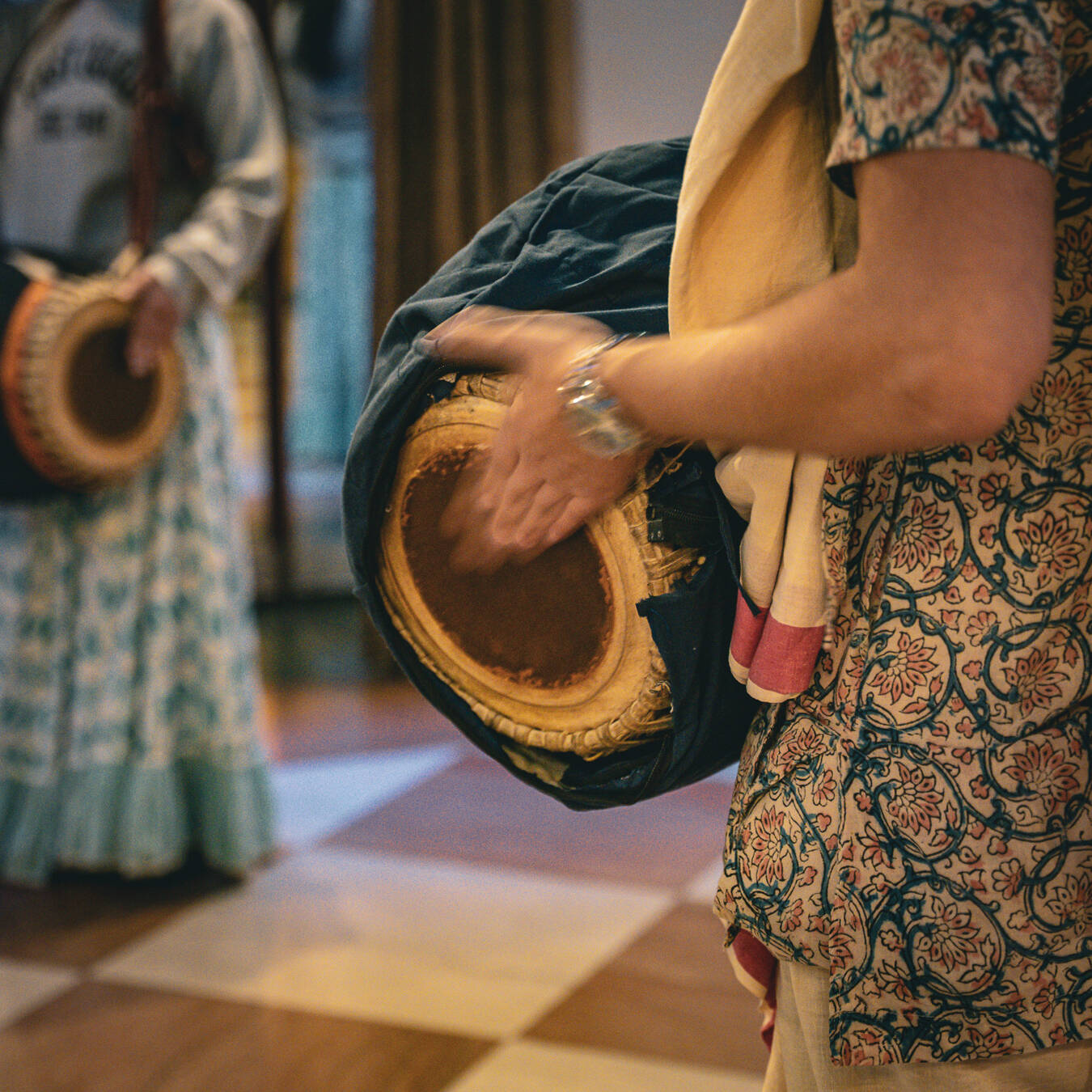 A close up of a hand drum being used during a ceremony with a second drummer in the background.